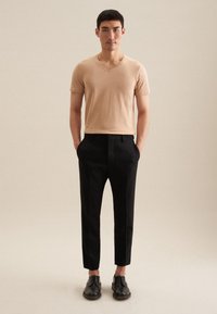 T-shirt beige clair à col en V associé à un pantalon noir ajusté et des chaussures noires. Textures lisses avec un design ajusté et des pantalons courtes.
