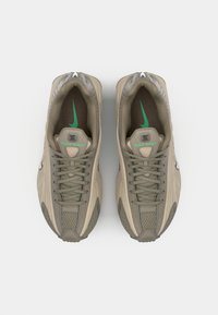 Baskets Nike Shox beiges avec tige texturée, accents verts et lacets. Comprend une languette rembourrée et un logo sur le côté et à l'avant.