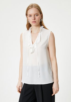 Weiße ärmellose Bluse mit einem Rüschenausschnitt, Spitze und Bindebänder am Hals, aus leichtem, durchsichtigem Stoff.