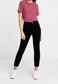 Svarta kordjeans med slim fit och kort längd, i kombination med en röd och vit randig t-tröja med kort ärm och vita sneakers.