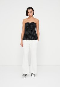 Svart, stroppeløs topp med hvite polka dots, med en sløyfe i midjen. Kombinert med hvite, vide bukser og svarte joggesko.