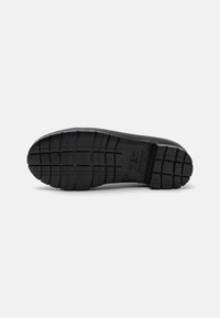 Black rubber shoe sole with deep tread patterns, featuring a logo and size marking embedded near the heel for traction and durability.