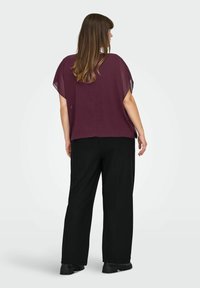 Top fluido bordeaux con maniche corte e trasparenti abbinato a pantaloni neri a gamba larga. L'outfit presenta una vestibilità rilassata e una consistenza morbida.