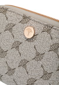 Close-up van een grijze, gestructureerde stoffen etui met donkere bloemenpatronen, een gouden ronde knop met een gegraveerde distel en een gouden ritssluiting langs de bovenrand.