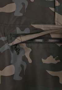 Kamuflázs mintázatú szövet sötétzöld, bézs és szürke árnyalatok keverékével. Cipzáras zseb, húzózsinórral. Texturált felület.