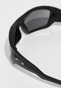 Černé sluneční brýle s elegantním rámem, tmavými skly a zlatým akcentem po straně. Vyznačují se hladkým povrchem a ergonomickým designem.