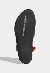 Sola de sapato de escalada em borracha preta com acabamento texturizado; apresenta o logótipo "STEALTH" e uma tampa de puxar vermelha brilhante de um lado.