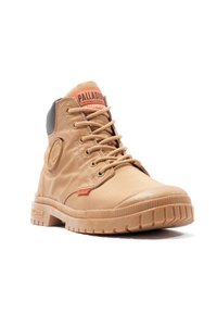 Tan waterproof boot with a textured fabric upper, lace closures, orange brand tag on the tongue, and rugged rubber sole with prominent tread.