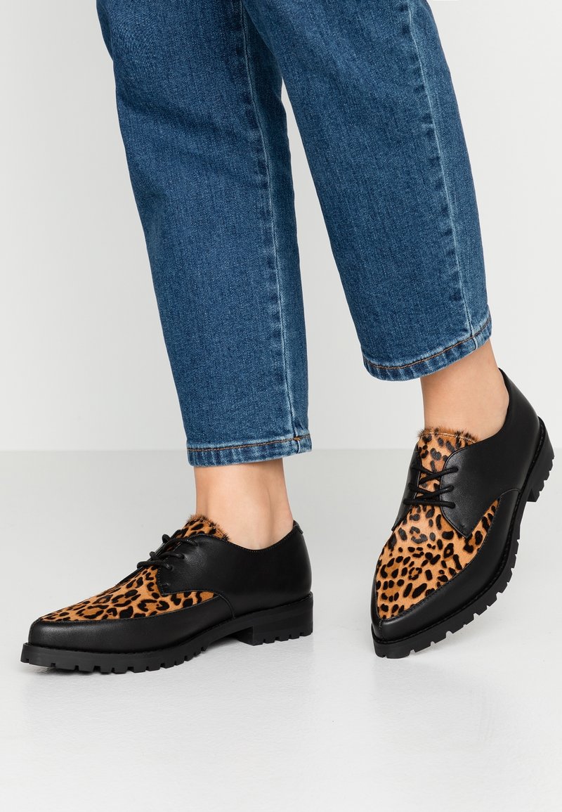 Chaussures en cuir avec un talon noir et un laçage à l'avant, dotées d'un dessus à imprimé léopard. Semelle épaisse et texturée pour une meilleure adhérence.