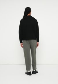 Svart strikket genser, kort design, rund hals. Lyst grønne tapered bukser, med mansjett. Svarte sko med glansfull finish.