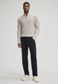 Pull-over tricot léger gris clair avec un col zippé, associé à un pantalon bleu marine foncé et des baskets crème. Texture lisse et design ajusté.