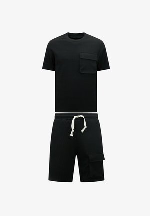 Zwarte gebreide t-shirt met korte mouwen en een borstzakje, gecombineerd met bijpassende zwarte shorts met een zijzak en een witte koord.