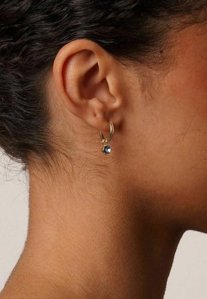 Goldene Creole mit einem kleinen blauen Edelsteinanhänger, ausgestattet mit einer glatten Oberfläche und einem schlichten Design, getragen am gepiercten Ohr.