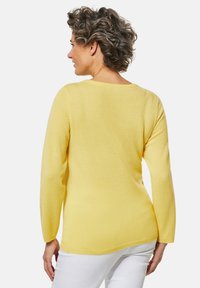 Gelber langärmeliger Pullover mit rundem Ausschnitt und strukturierter Oberfläche. Hat einen lockeren Schnitt und seitliche Schlitze für zusätzlichen Komfort.