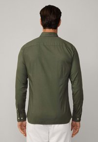 Camicia a maniche lunghe verde oliva con colletto, polsini con bottoni e una texture liscia, caratterizzata da una vestibilità aderente e dettagli minimi.