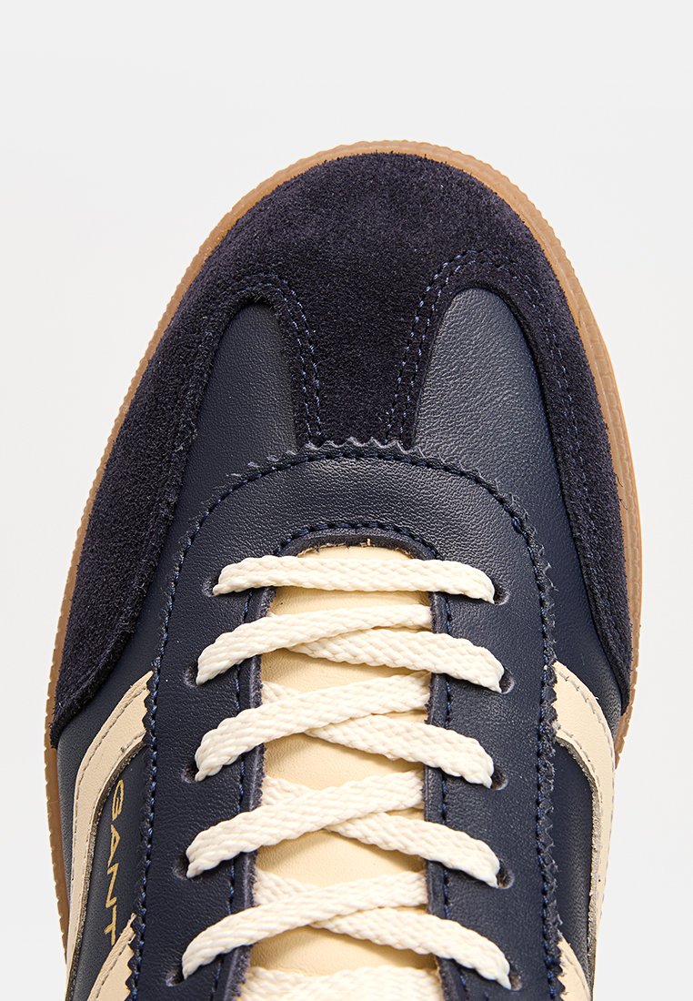 Marineblaue Sneaker mit cremfarbenen Schnürsenkeln und beigen Akzenten, mit einer Veloursleder-Spitze und einer Gummisohle, Nahaufnahme von oben.