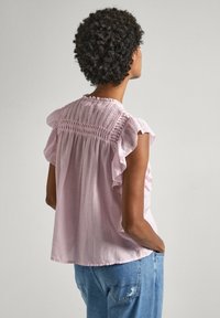 Blouse rose clair à manches courtes avec des accents volants et un dos smocké texturé. Tissu lisse ; coupe décontractée. Portée avec un jean en denim.