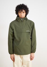 Olivgrüner Windbreaker mit halbseitigem Reißverschluss, elastischen Bündchen und einer Vordertasche. Leichtes Material mit glatter Textur.