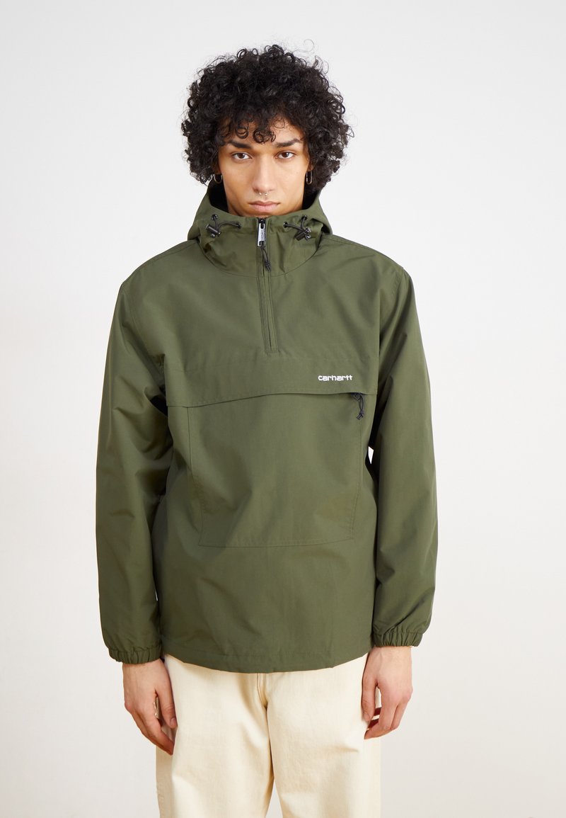 Olivgrüner Windbreaker mit halbseitigem Reißverschluss, elastischen Bündchen und einer Vordertasche. Leichtes Material mit glatter Textur.