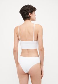 Bralette blanc côtelé et bas de bikini assortis. Le bralette a des bretelles fines et un ourlet droit ; le tissu semble lisse et doux.