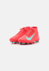 Nike nogometne kopačke u svijetlopinkastoj boji s teksturiranim gornjim dijelom, s velikim mint zelenim Swoosh logotipom i tirkiznim kramponima na potplatu.