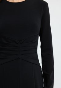 Schwarzes langärmeliges Kleid mit enganliegendem Oberteil, gerafftem Taillierung, glattem Stoff und rundem Halsausschnitt.