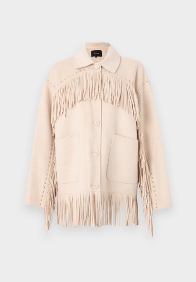 Μπεζ μάλλινο σακάκι με φράντζα κατά μήκος του στήθους και της κάτω πλευράς, υπερμεγέθεις τσέπες και διακοσμητικές ακίδες στους ώμους.