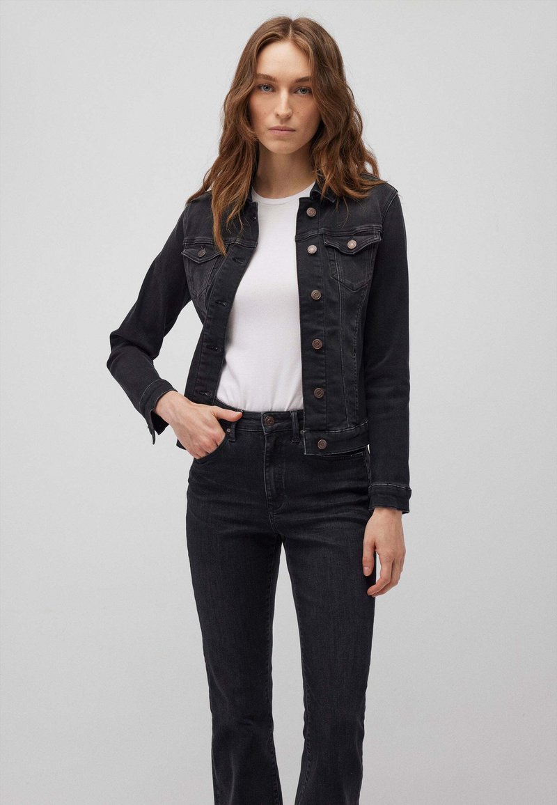 Giacca di jeans nera con chiusura a bottoni, due tasche sul petto e maniche lunghe, abbinata a jeans di jeans neri e una maglietta bianca.