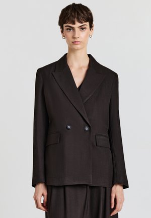 Blazer noir croisé avec des revers pointus, deux poches avant et des accents de boutons. Le tissu a une finition lisse et légèrement texturée.