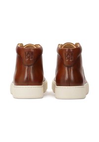 Zapatillas altas de cuero marrón con suela de goma crema, que presentan un logo en relieve en la parte trasera y una textura suave.