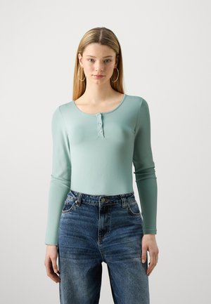 Lyseblå langermet henley-topp med rund hals og tre knapper, kombinert med mellomblå høy midje jeans.