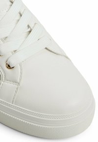 Sneaker bianco con tomaia in pelle sintetica liscia, punta rotonda, lacci bianchi, occhielli dorati e suola in gomma texturizzata con leggere scanalature.