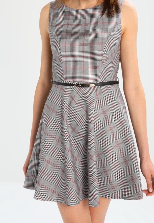 Robe grise sans manches à motif écossais rouge et noir, corsage ajusté, jupe évasée, et fine ceinture noire avec boucle métallique à la taille.