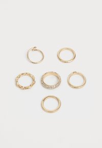 Conjunto de anéis de ouro, apresentando vários designs: uma corrente, uma banda lisa e uma com pedras transparentes. Diferentes texturas e acabamentos estão presentes.