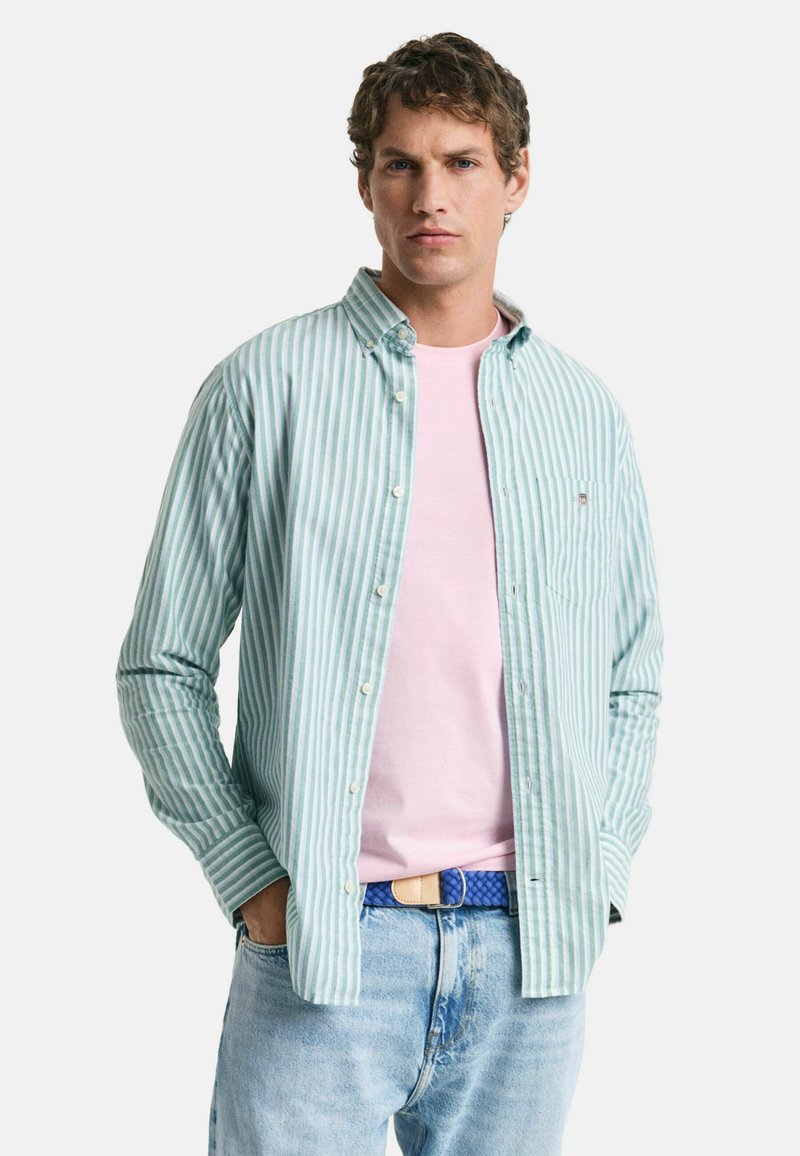 Camisa a rayas en azul claro y blanco, superpuesta sobre una camiseta rosa. Combinada con jeans azul claro y un cinturón trenzado azul.