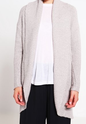 Cardigan grigio chiaro lavorato a maglia con apertura frontale, tessuto testurizzato, maniche lunghe e vestibilità comoda, indossato sopra una camicia bianca.