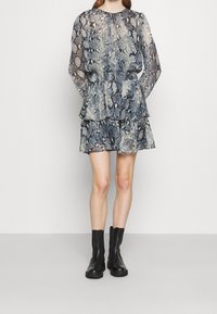 Vrstvené šaty s dlouhým rukávem a modro-krémovým hadím potiskem. Vyrobené z lehkého materiálu, mají vypasovaný pas a rozšířenou sukni.