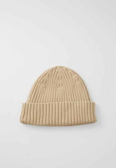 Bonnet en tricot beige avec texture côtelée et revers roulé. Présente un motif de couture vertical sur la couronne. Léger et flexible.