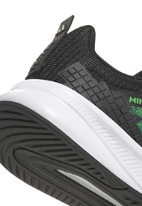 Chaussure de sport noire avec dessus en tissu texturé, accents verts et semelle intermédiaire blanche. Dispose d'une semelle extérieure en caoutchouc à motif pour une meilleure adhérence.