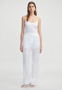 Witte, luchtige broek met verticale gaasstrepen en zilveren studs. Gecombineerd met een aansluitend wit tanktop en sandalen met bandjes.