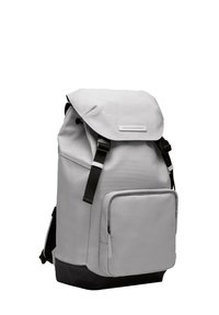 Sac à dos en tissu gris avec une fermeture à rabat, des bretelles réglables, une poche zippée à l'avant et une base noire. Texture lisse et design minimaliste.