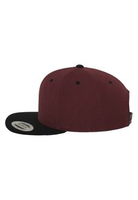 Cappellino da baseball bordeaux con visiera piatta nera. Realizzato in tessuto con una texture liscia, presenta fori di ventilazione e una chiusura regolabile a scatto.