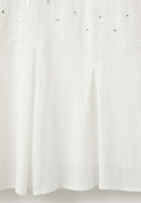 Tissu blanc texturé avec broderie florale et détails à œillets au-dessus de deux plis devant sur une jupe ou une robe.