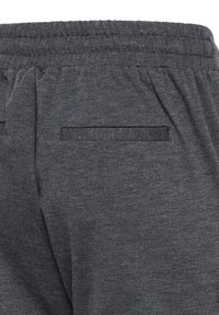 Pantalon de survêtement en tissu gris foncé avec taille élastique et une seule poche passepoilée horizontale à l'arrière.