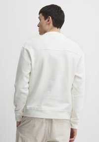 Sudadera blanca de manga larga, con puños acanalados y cuello redondo. Textura suave, corte holgado y diseño minimalista.