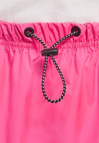 Poignées de taille rose avec un cordon rayé noir et blanc. Dessus élastique avec des œillets noirs pour l'ajustabilité. Matériau lisse et léger.