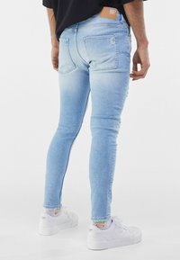 Ljusblå smala jeans med en blekt mönster, med trasiga detaljer och en brun läderlapp vid midjebandet. Bärs med vita sneakers.