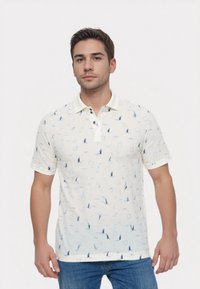 Kortærmet polo shirt i creme med blå sejlb�åde og cirkulære mønstre, kontrasterende krave og to-knaps placket. Tekstureret bomuldsstof.