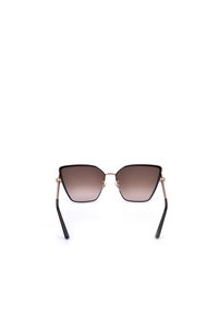 Lunettes de soleil en métal noir et or avec de grandes verres bruns dégradés légèrement en forme d'œil de chat et des branches fines sur fond blanc.