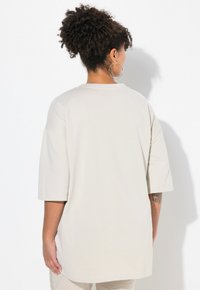 Helles beigefarbenes Oversized-T-Shirt mit kurzen Ärmeln und rundem Ausschnitt, aus weichem Material gefertigt. Verfügt über eine entspannte Passform und eine dezente Textur.